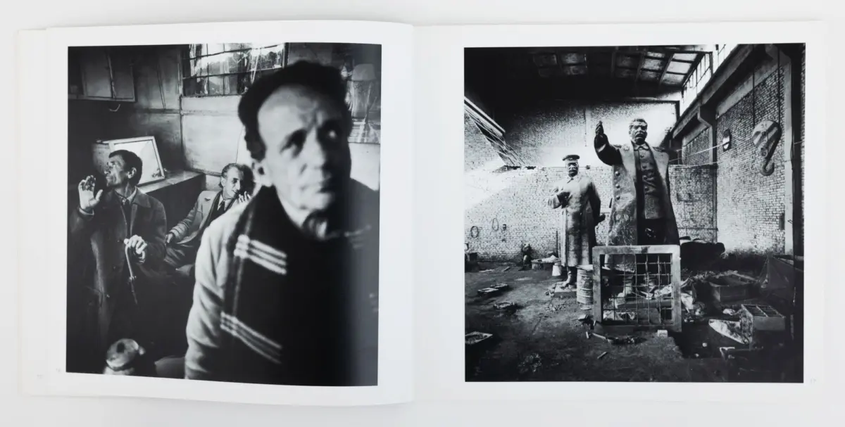 Left page: three people in a dim workshop; blurred foreground figure. Right page: industrial ruin with two statues, one raised arm amid debris.