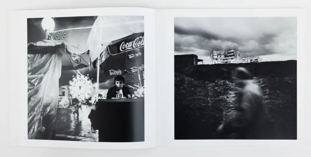 Two-page black-and-white spread: left a street market stall under Coca-Cola umbrellas with a vendor; right a ruined hilltop apartment block under stormy skies.