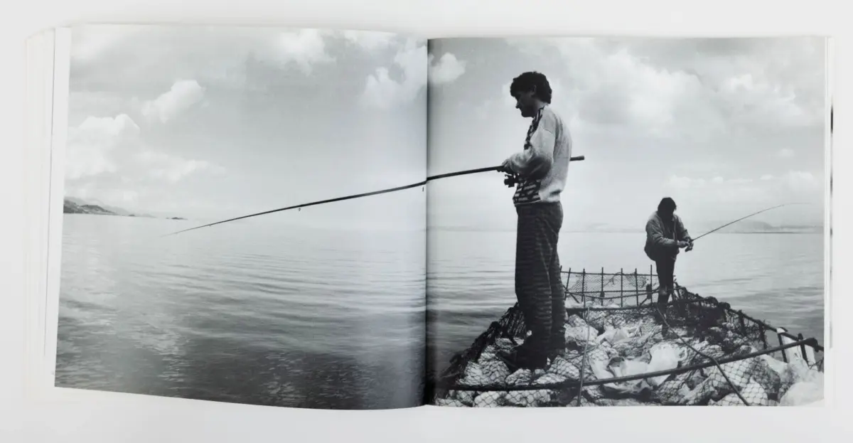 Two anglers fishing from a rocky jetty into calm water under a cloudy sky.