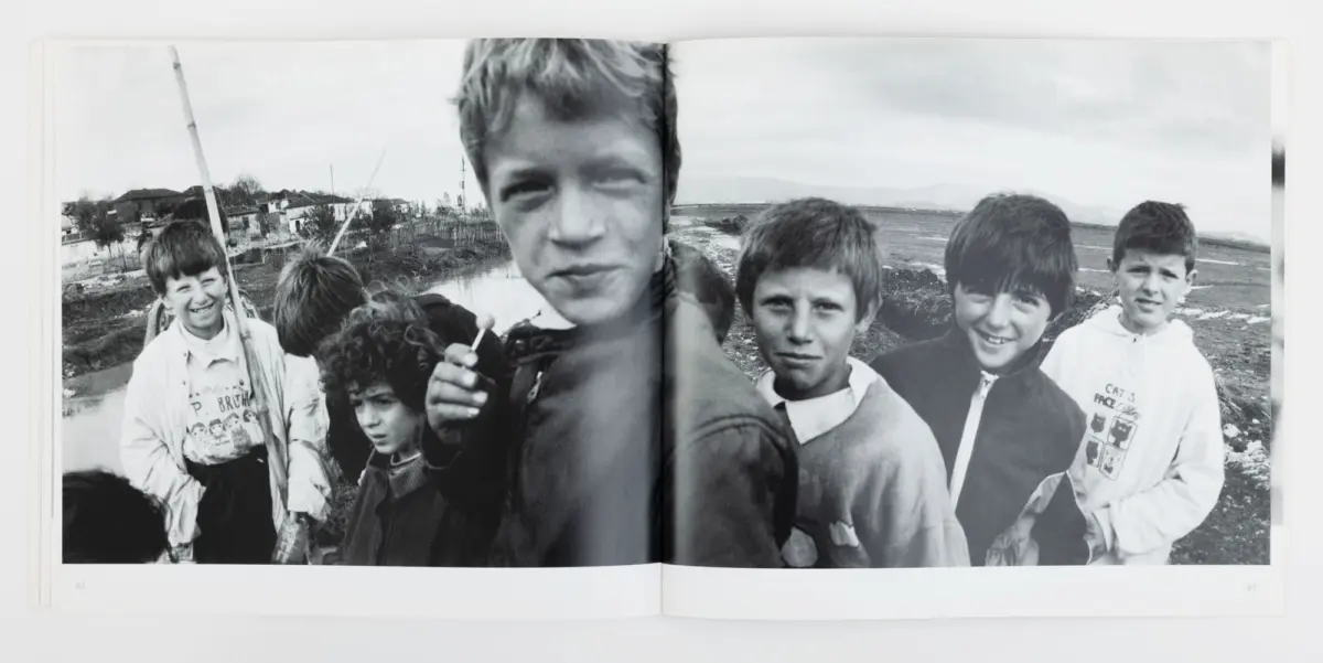 Group of boys outdoors on a muddy riverbank, posing for a photo; central boy stands closest to the camera.