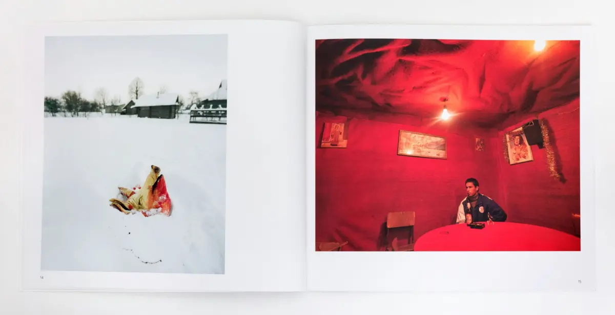 Two-page photo spread: left snow-covered village with a colorful cloth in the foreground; right man in a red-lit room seated at a round table.