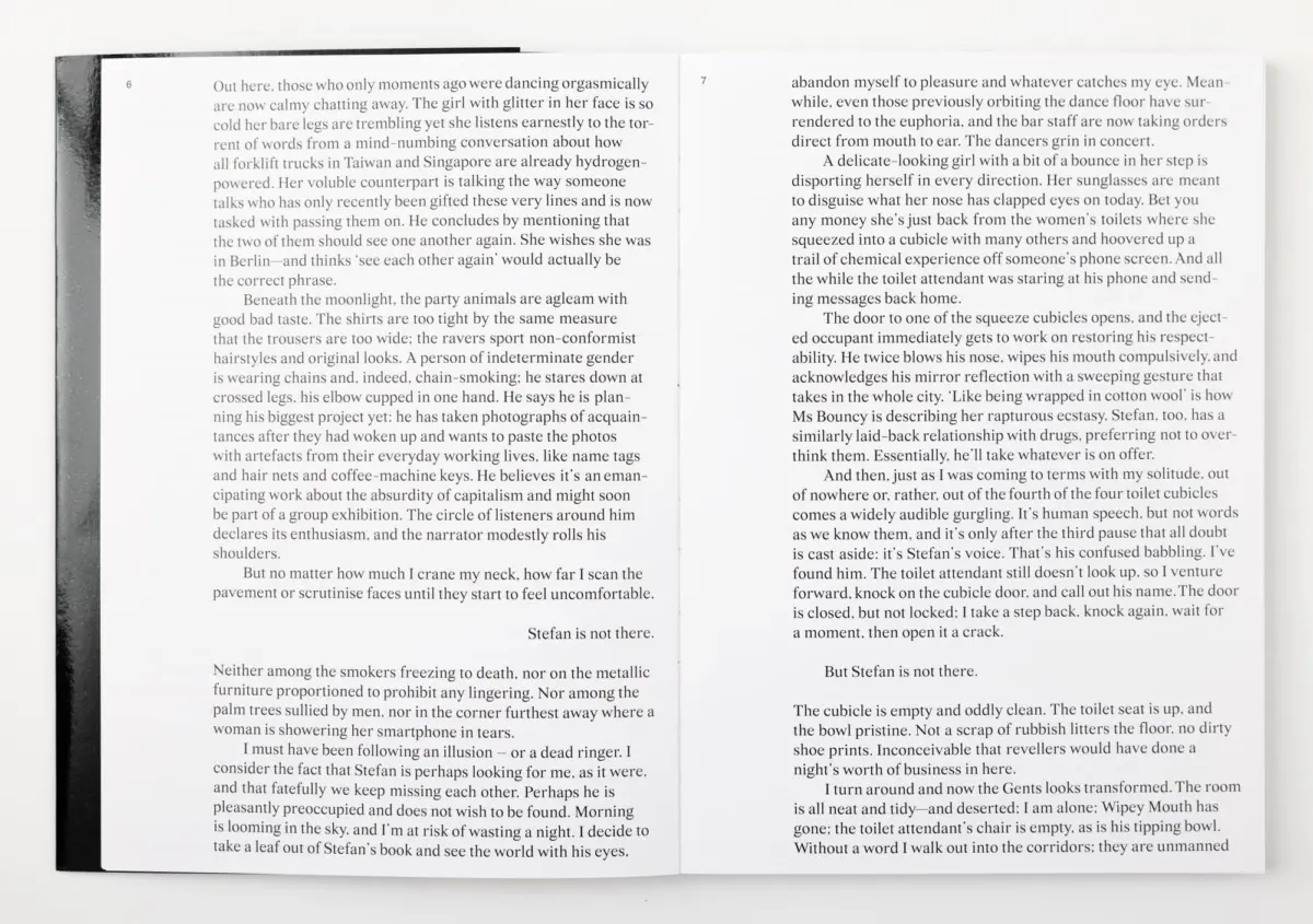 Open book with two pages of dense paragraphs on white paper; black spine visible on the left, resting on a white surface.