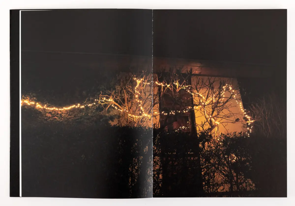 Open photo album spread showing a nighttime yard scene with warm string lights on leafless trees.
