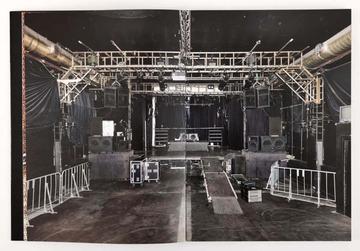 Overhead stage lighting truss with spotlights and loudspeakers above an empty stage; backstage setup in a venue.