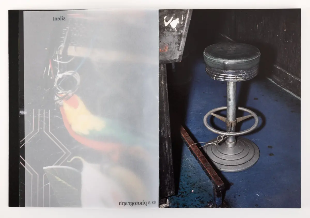 Round black leather swivel stool on a metal pedestal inside a dark cabinet; left page shows a faded circuit-pattern graphic.