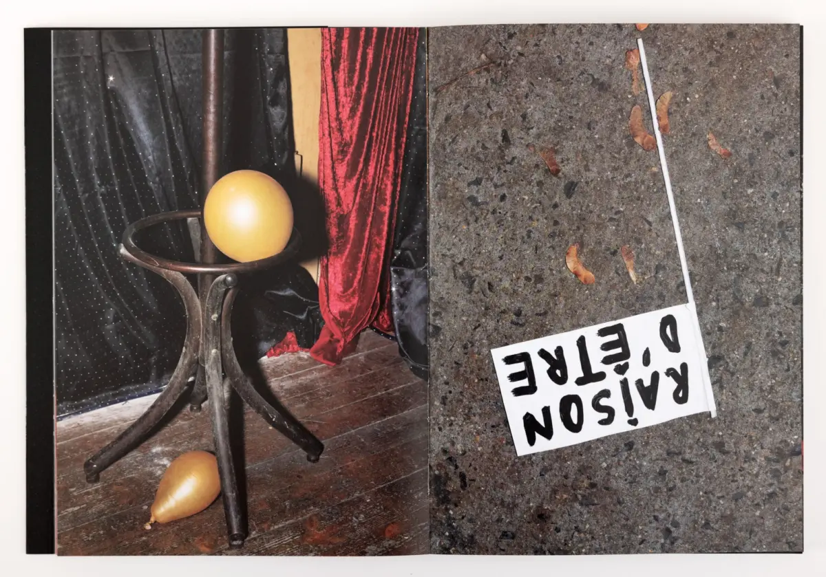 Yellow ball on a metal stool on a stage, with red velvet curtains; concrete ground with leaves and a tilted CAUTION sign.