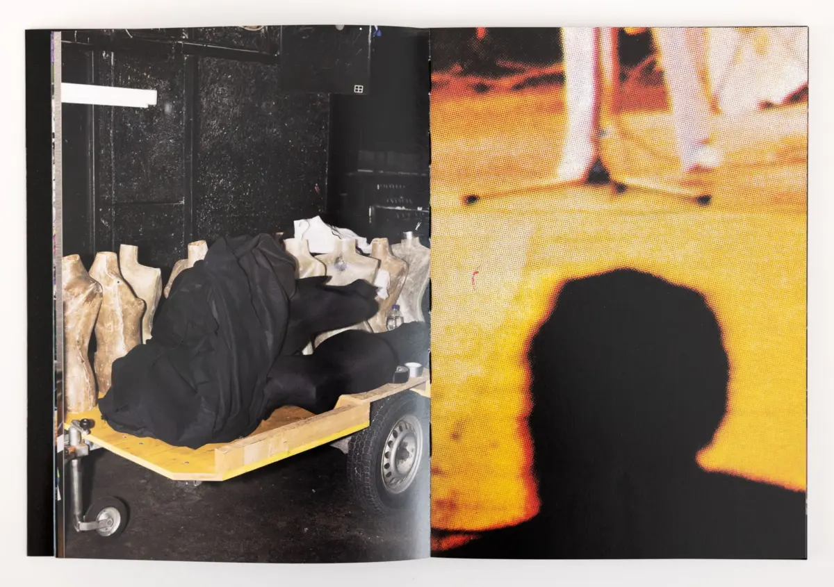 Left page shows mannequin torsos in black fabric on a wooden wheeled platform in a workshop; right page shows a bright orange poster.