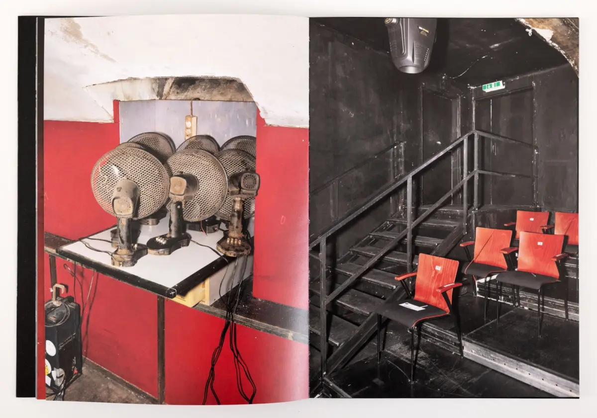 Theater interior, split view: left shows dusty pedestal fans on a red counter; right shows a black-walled auditorium with a metal railing and orange seats.