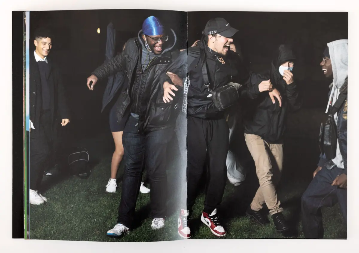 Diverse group of young adults walking and laughing together outdoors at night on grass.