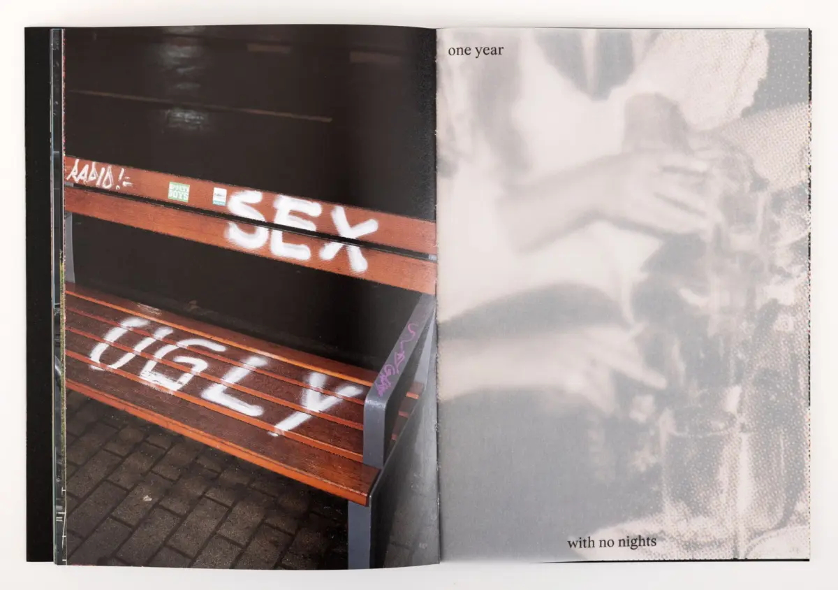 Open book spread showing graffiti-covered wooden bench with orange slats at night; left page dark, right page grayscale.
