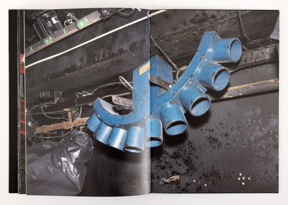 Blue metal pipe-fitting assembly with four cylindrical outlets on a dirty workshop floor.