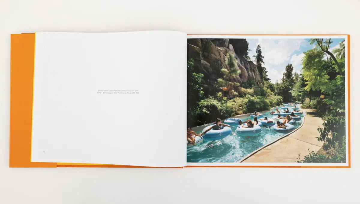Open photo book showing a tropical water-park scene on the right: people in blue inflatable tubes ride a lazy river amid rocks and palm trees.