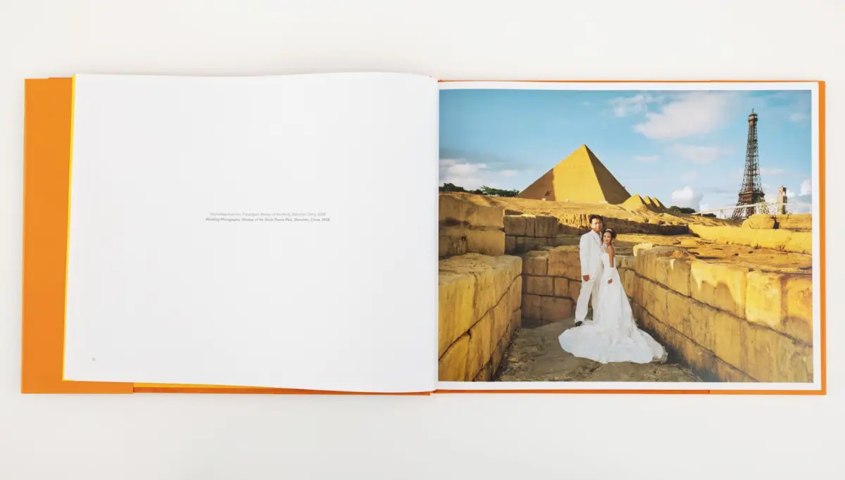 Wedding couple in white posing among ancient stone blocks, with a pyramid and Eiffel Tower replica in a sunny theme park.