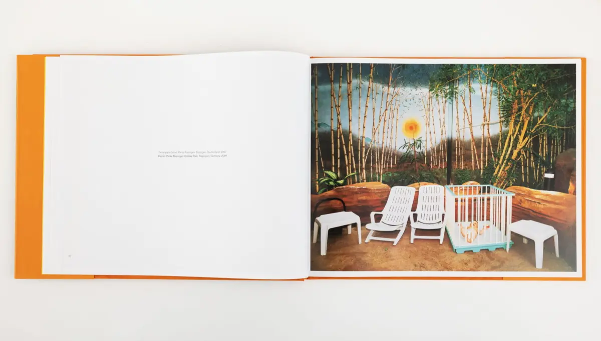 Baby in blue playpen on an outdoor patio with white plastic chairs and bamboo fence.