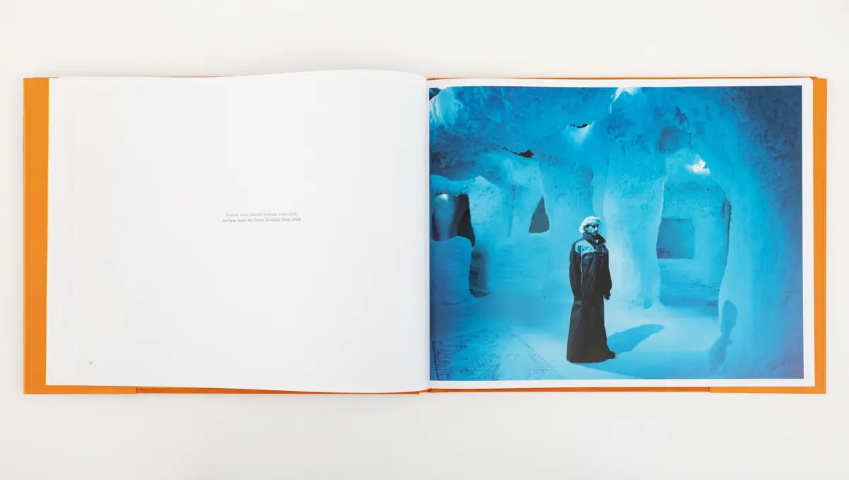 Open book with orange cover; right page features blue ice cave scene with a person in dark coat and white head wrap standing.