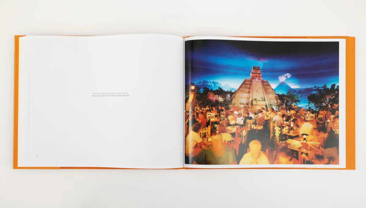 Night outdoor dining scene with many diners at tables; a large stepped pyramid and distant volcano rise in the blue sky.
