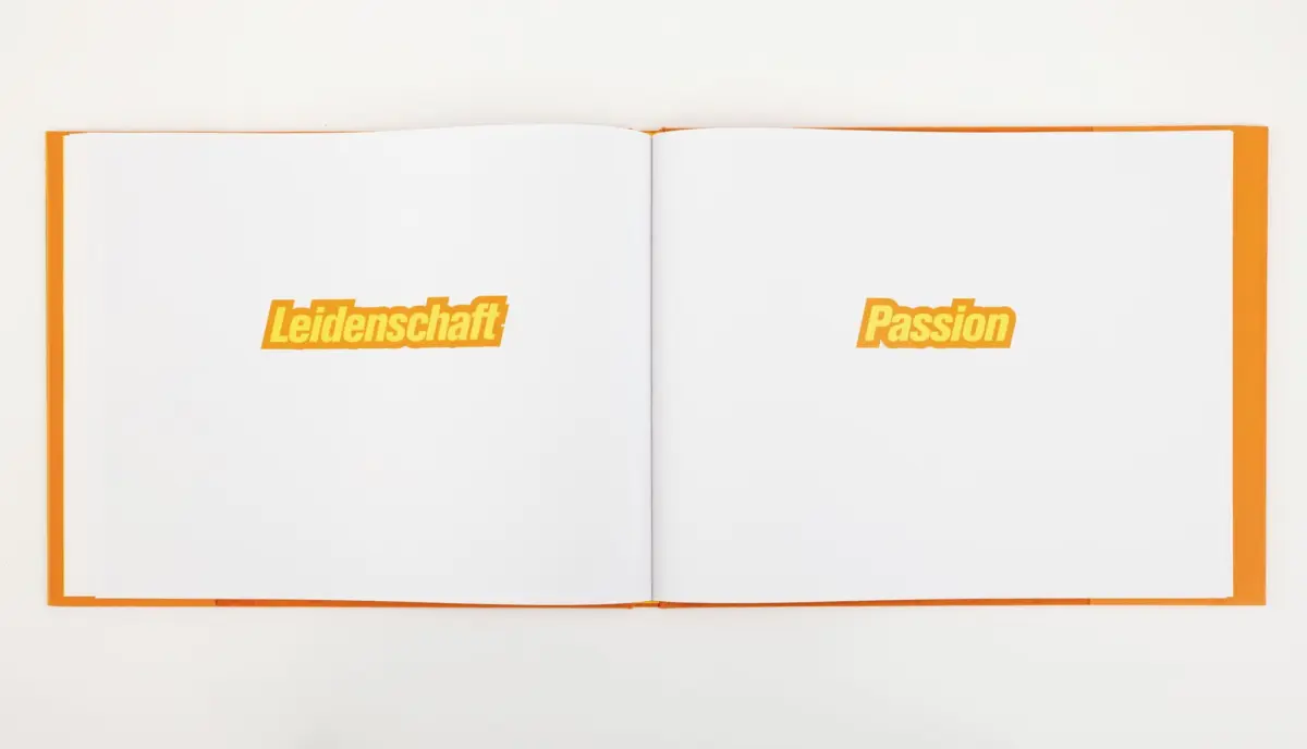 Open orange-cover hardcover; white pages display bold orange text: Leidenschaft on the left, Passion on the right.