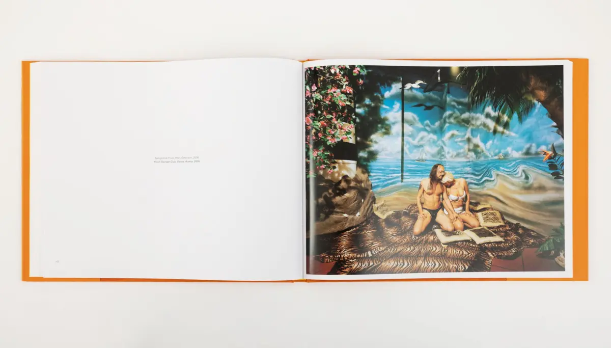 Two adults in swimsuits sit close together on a patterned rug in a tropical beach backdrop.