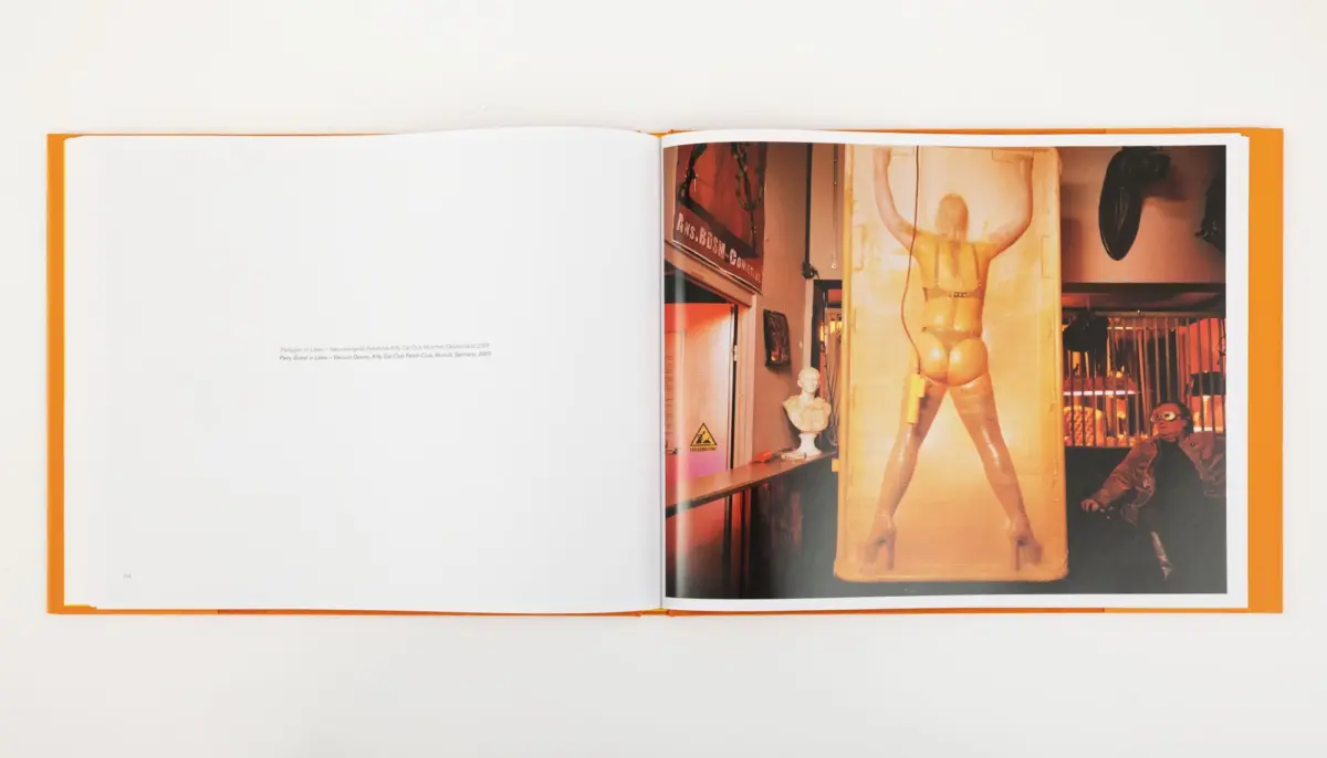 Open book with orange cover; right page shows a life-size yellow-suited mannequin with arms raised in a museum exhibit.