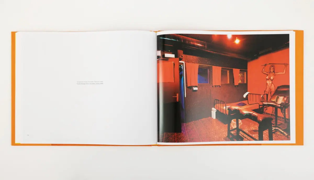 Open book displaying a red-lit interior photograph with a nude statue and lounge seating.