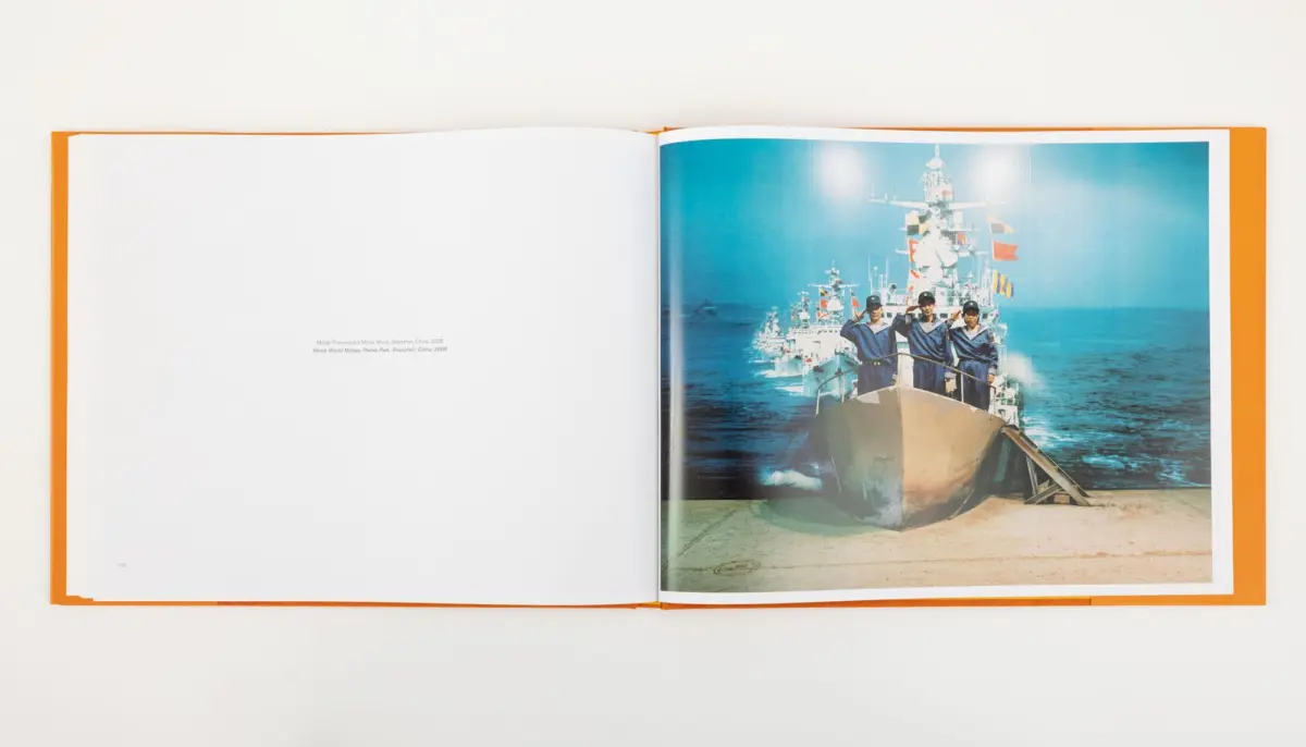 Open book page showing a naval warship at sea with three sailors on the bow saluting; flags on the mast.