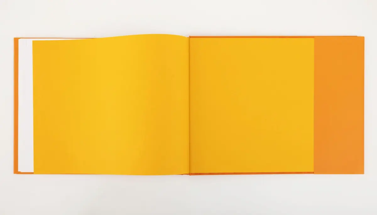 Open book with bright yellow pages and orange cover edge, laid flat on a white surface.