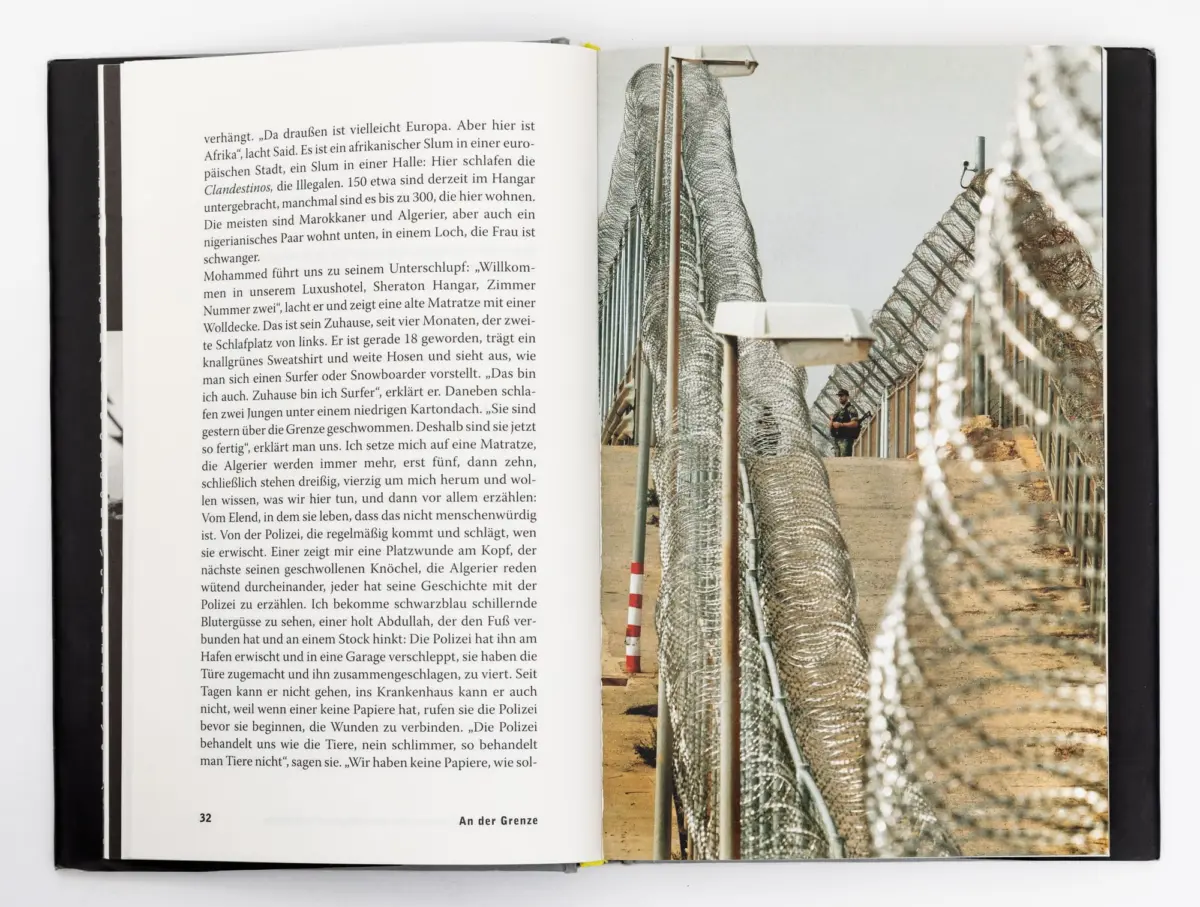 Open book with a desert border fence: coiled barbed-wire along a security barrier, a soldier standing near the fence.