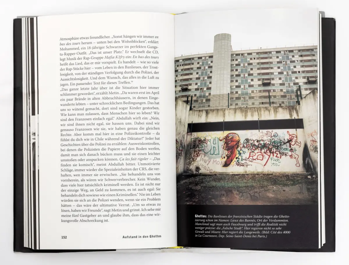 Open book with left page of German text and right page showing a graffiti-covered wall in front of a tall apartment building.