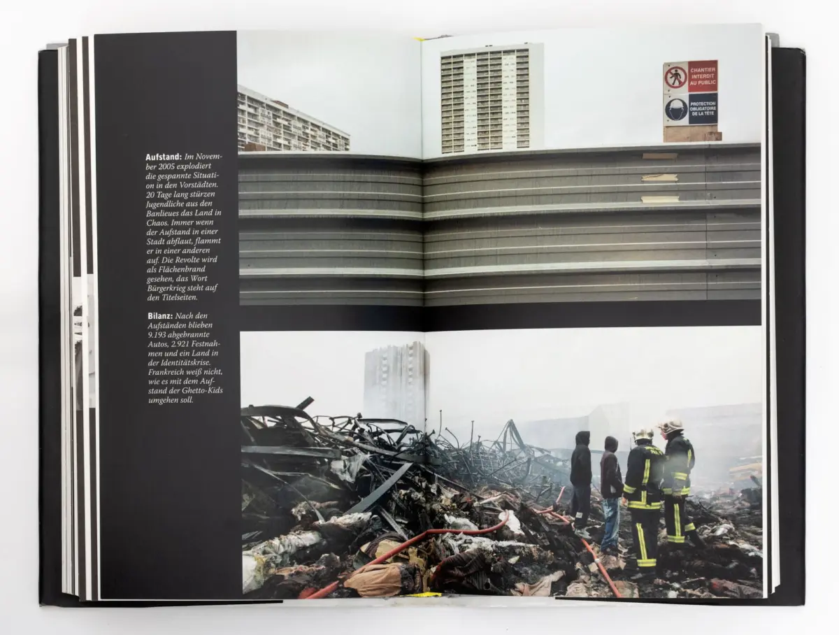 Firefighters in yellow gear examine rubble at an urban disaster site with high-rise buildings in the background.