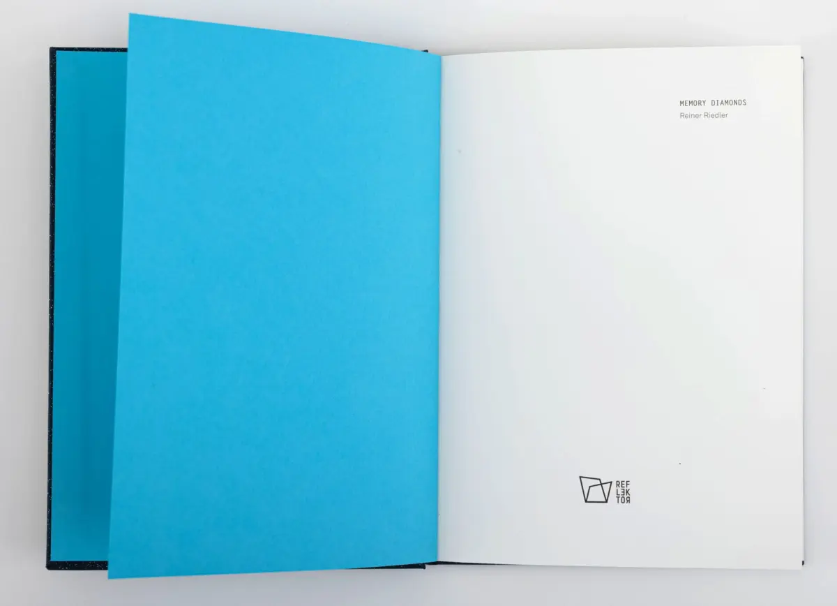Open book, vivid blue left page and white right page; text reads MEMORY DIAMONDS by Reiner Riedler, logo bottom right.