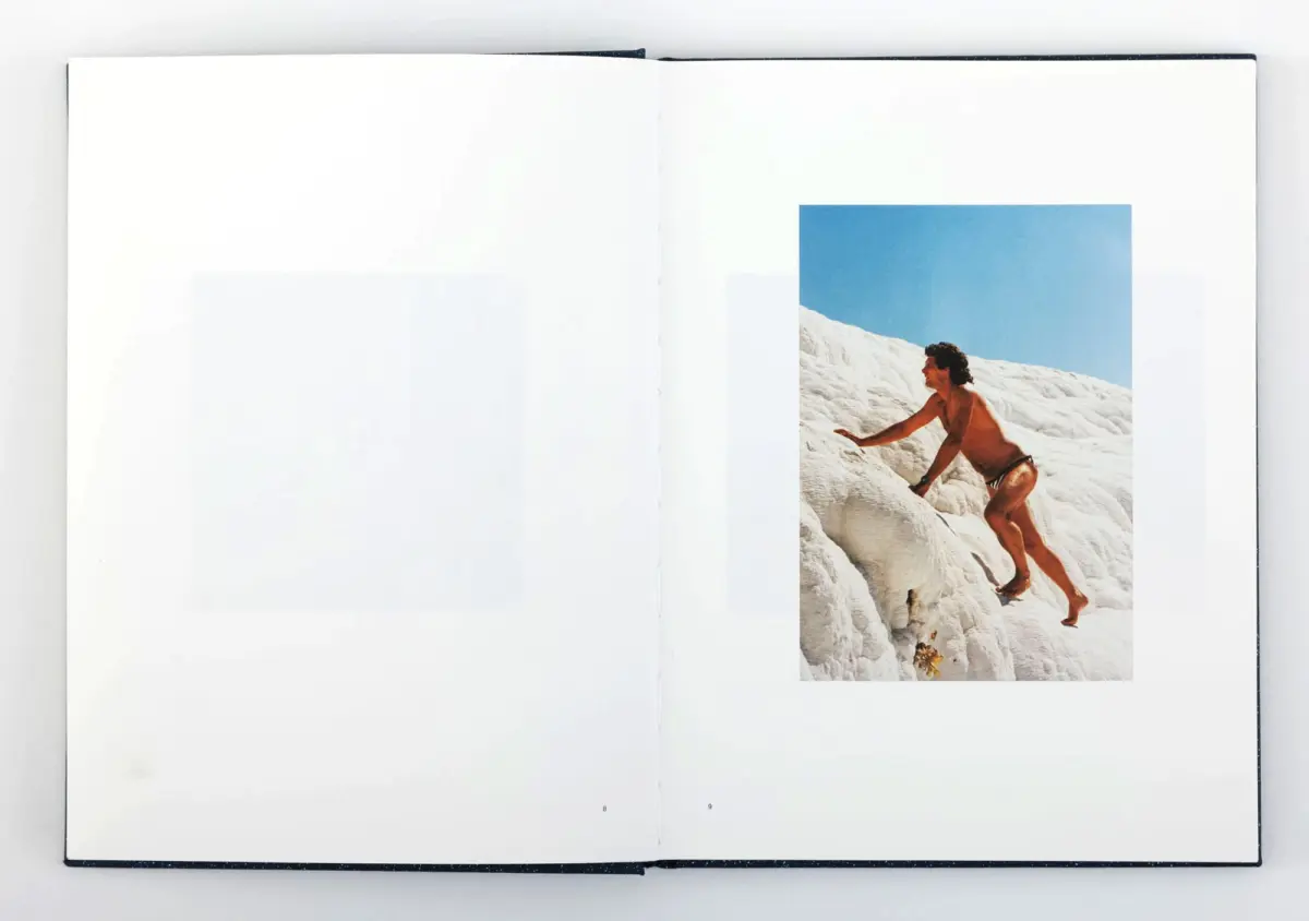 Bare-chested person climbing a snowy rocky slope under a clear blue sky.