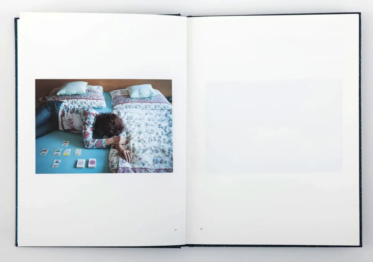 Person lying on bed under a floral quilt, laying out tarot cards on a blue sheet.