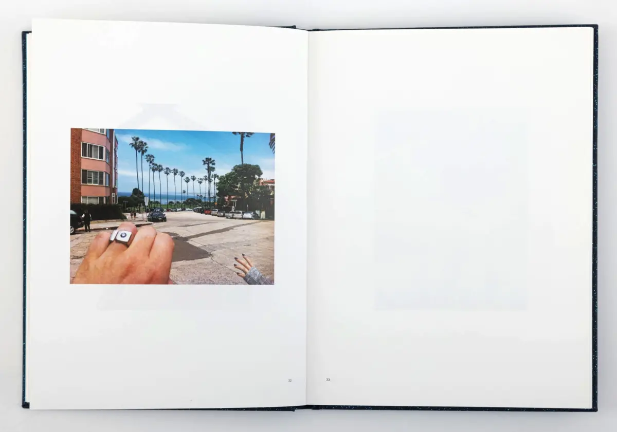Open book showing a pasted photo of a palm-tree-lined coastal street; two hands hold the image.