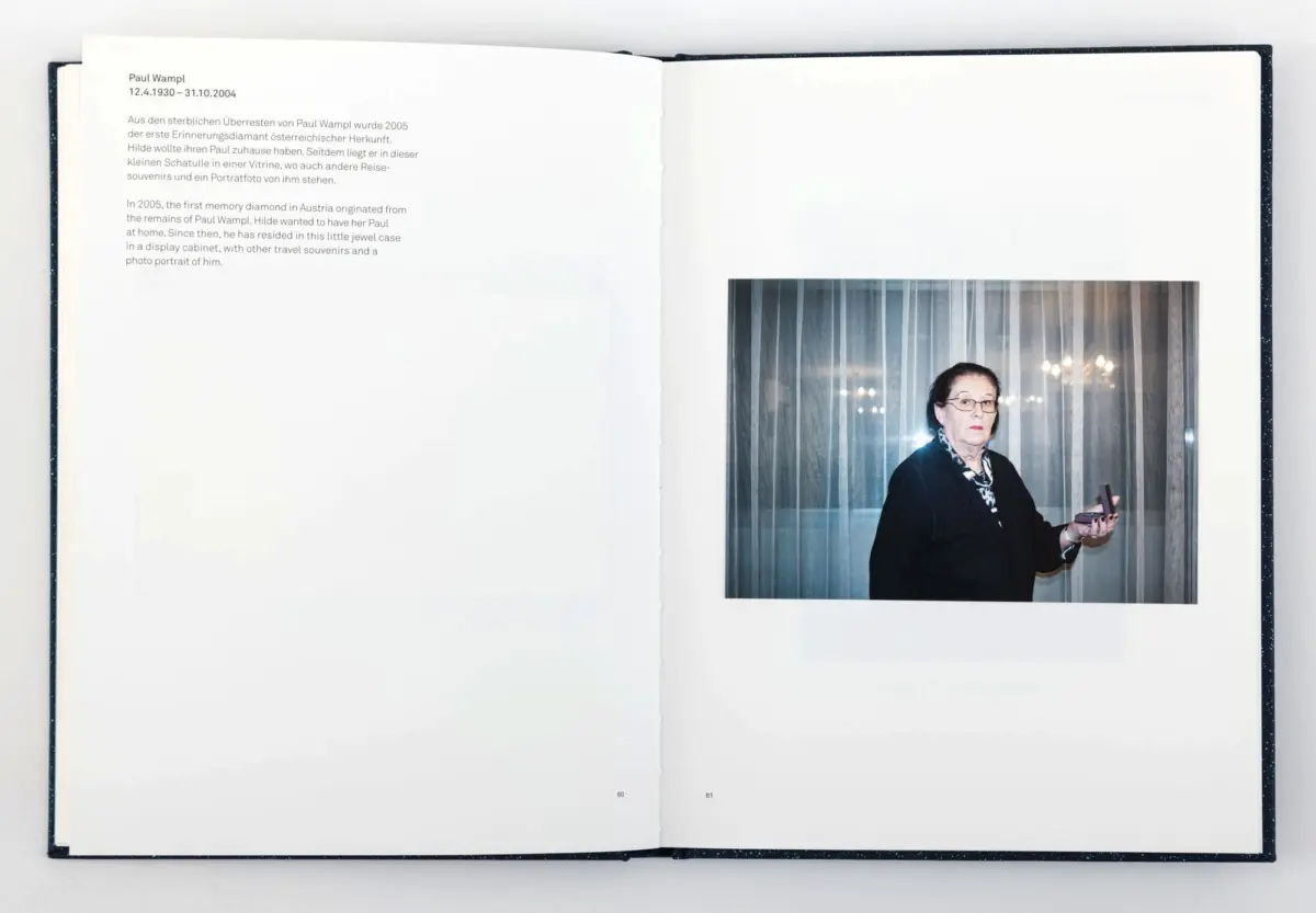 Open book spread; left page with text, right page shows an elderly person in dark clothing holding a pink object near striped curtains.