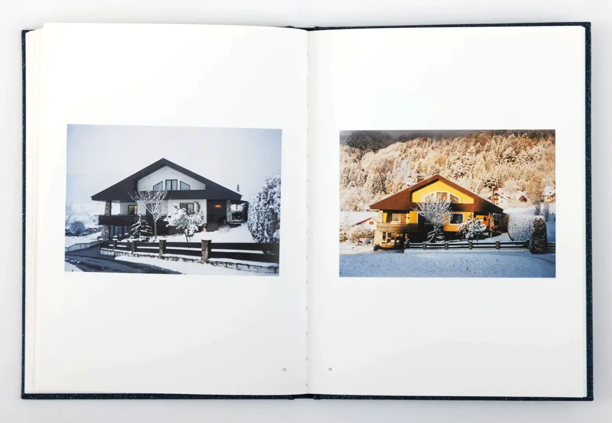 Open photo book showing two snowy houses: left modern white house with dark roof, right brown alpine-style home among snow-covered trees.