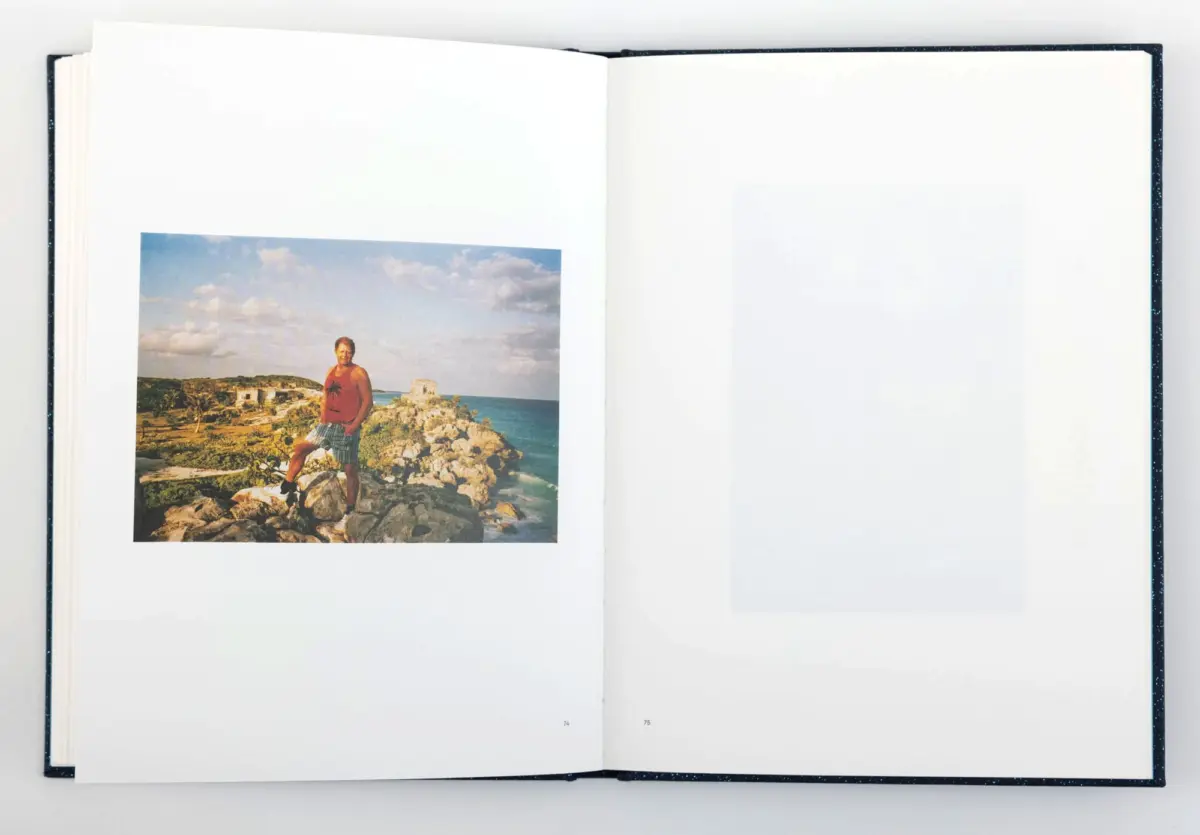Photo of a person standing on a rocky coastal shore, in an open book; wearing a red tank top and plaid shorts.