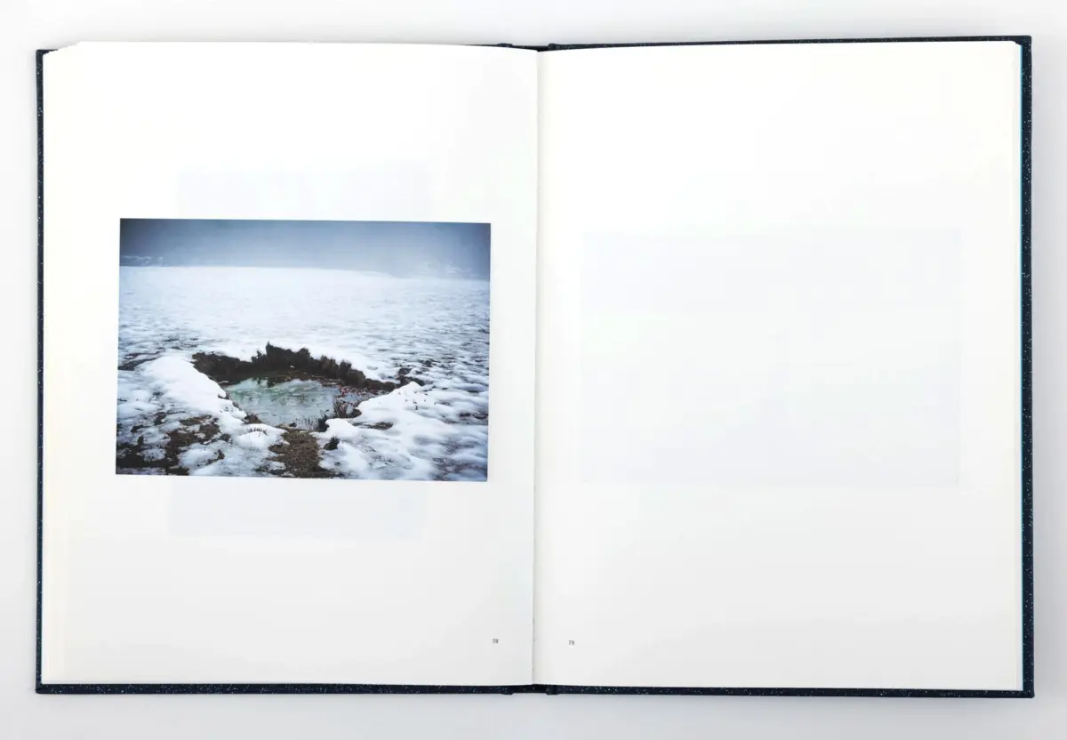 Open book displaying a photo of a snow-covered rocky coastline with a calm sea.