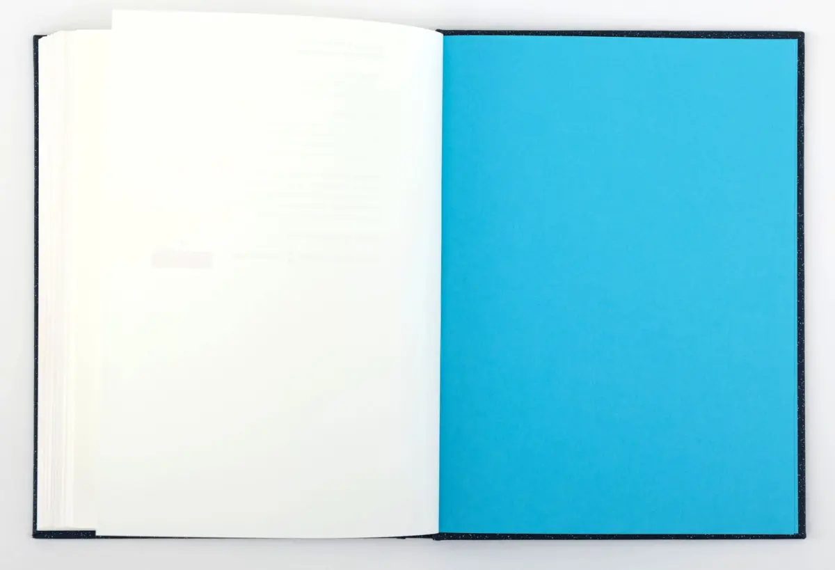 Open hardcover book with white left page and bright blue right page, laid flat on a white surface.