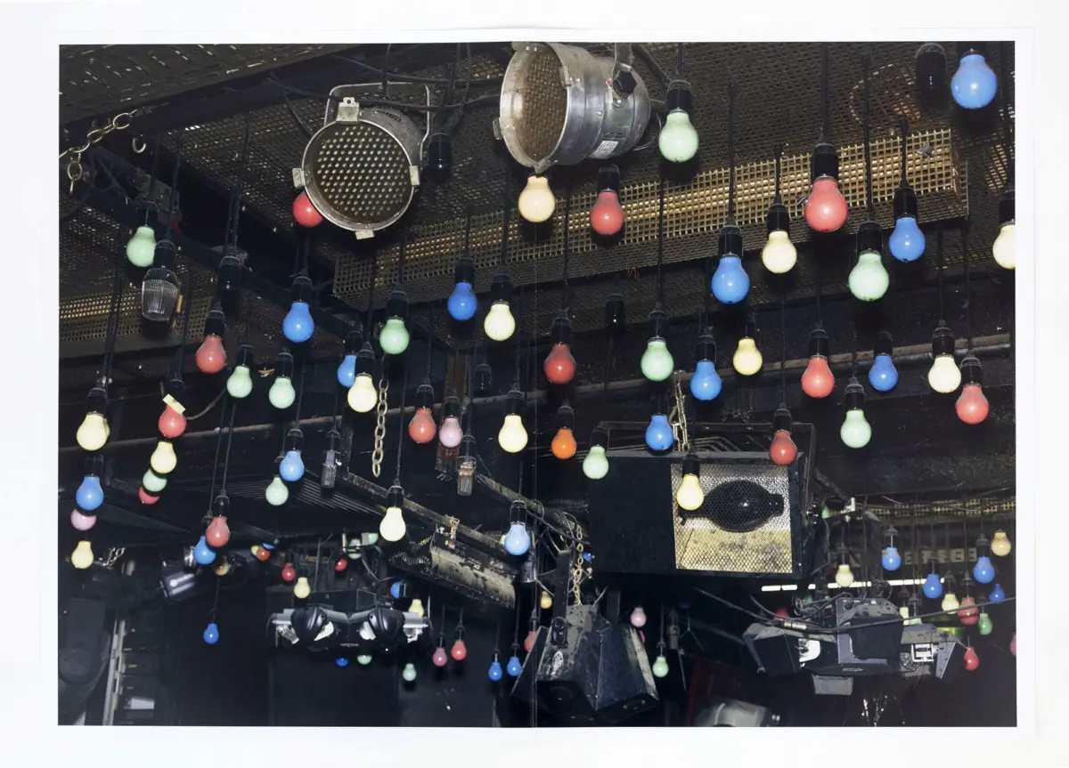 Colorful incandescent bulbs hanging from a theater lighting grid above a stage.