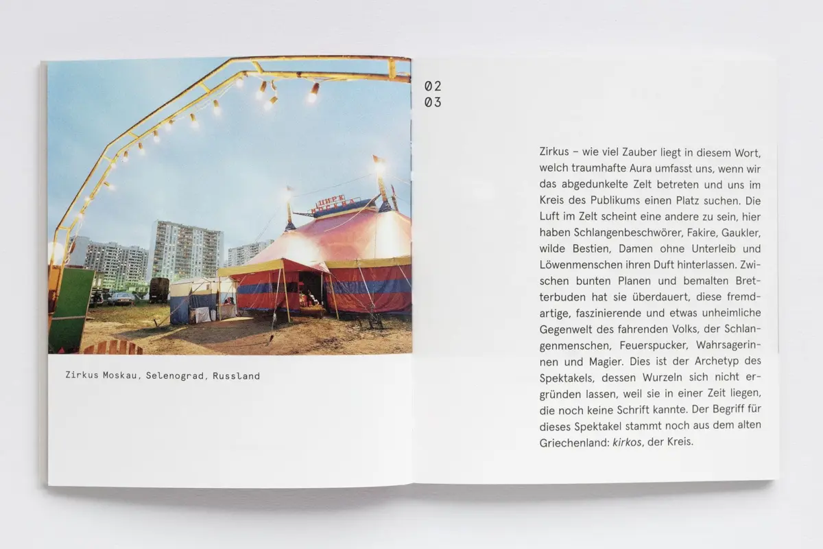 Open book with a photograph of a striped circus tent on a fairground, string lights overhead, and high-rise buildings in the background.