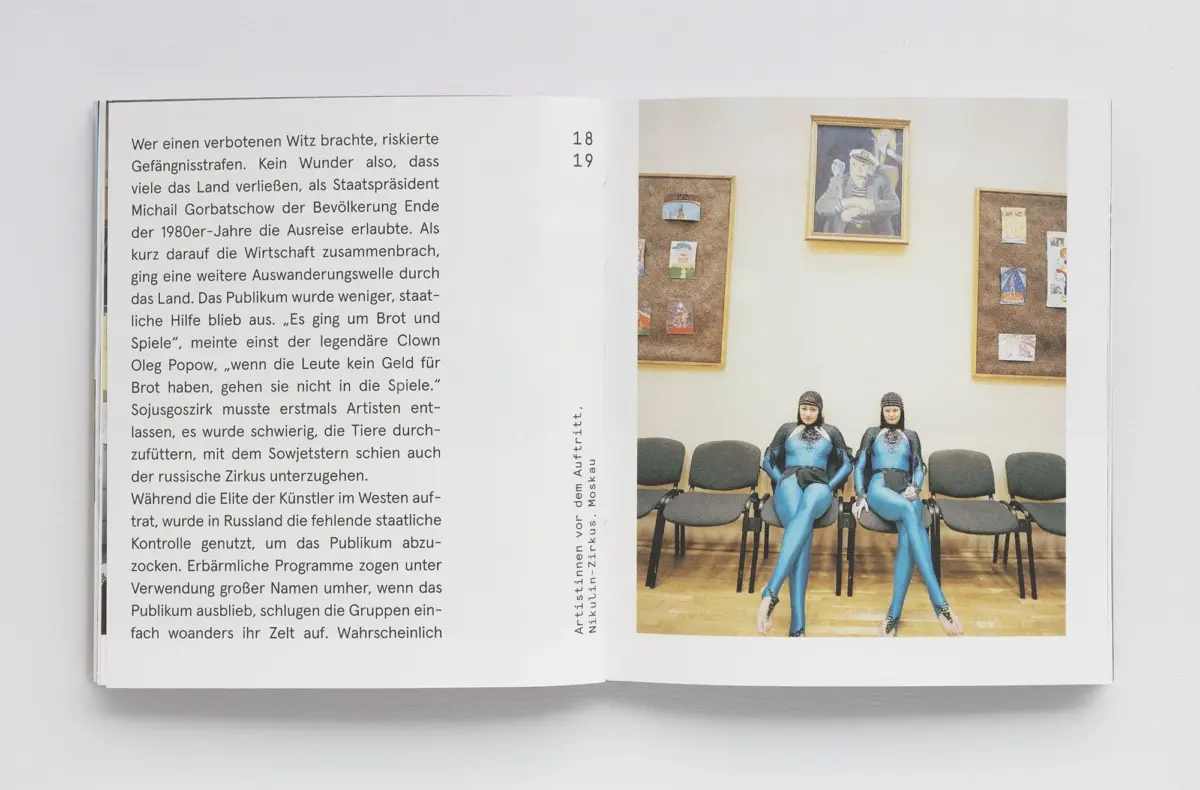 Two blue-clad performers sit on chairs in an art-gallery room with framed pictures.