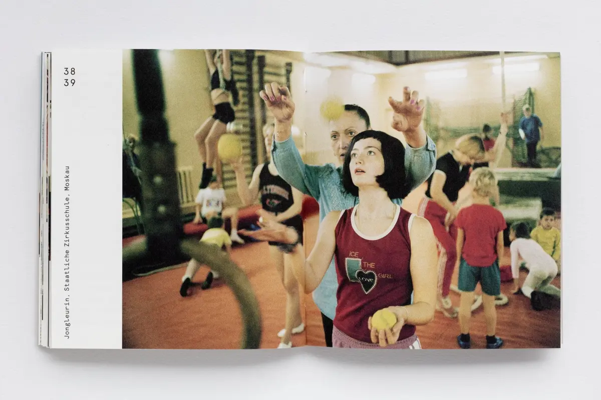 Young girl in a maroon tank top holding a yellow ball in a gym class with peers.