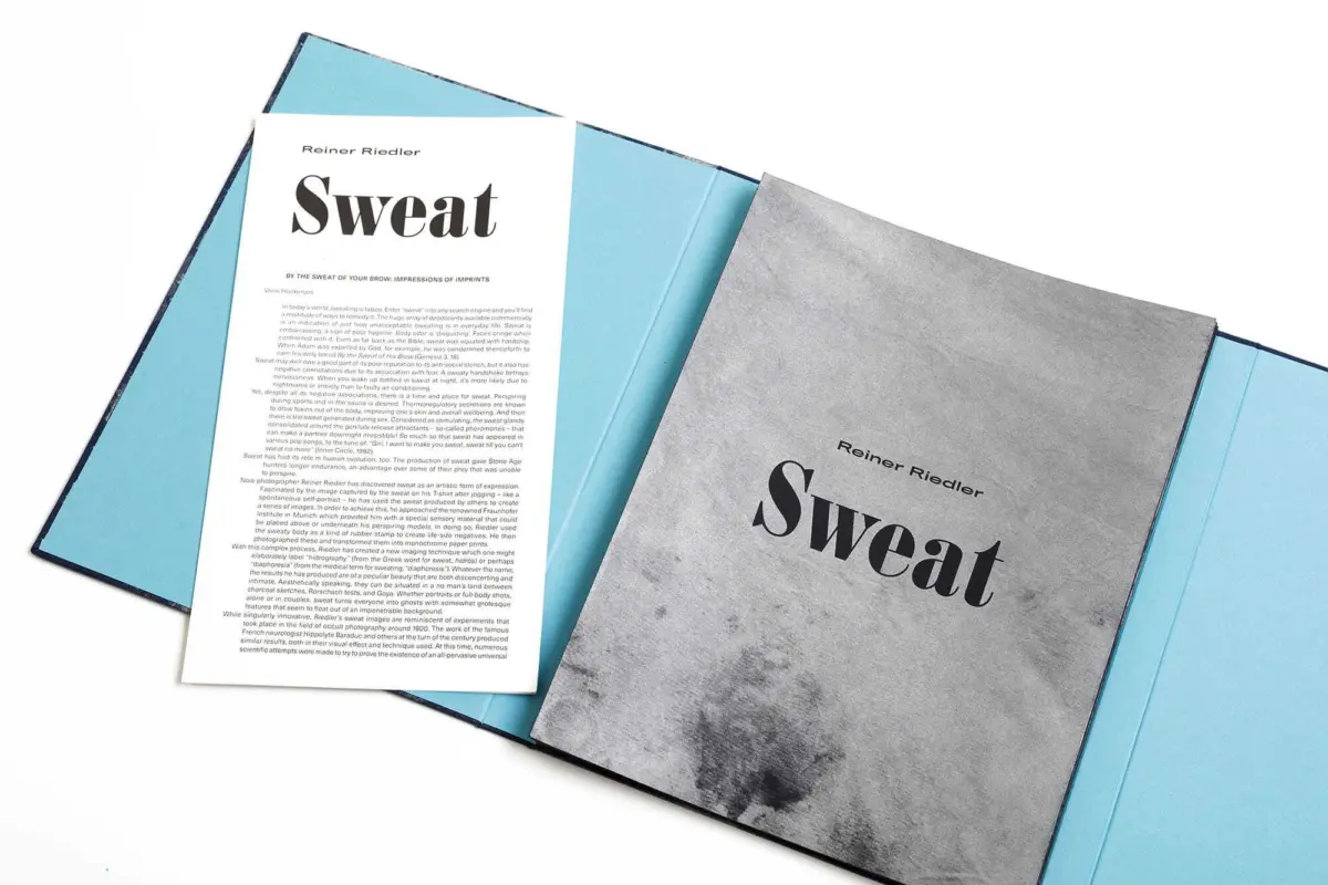 Two Sweat publications open on a light blue folder; one gray cover, one white page with dense text.