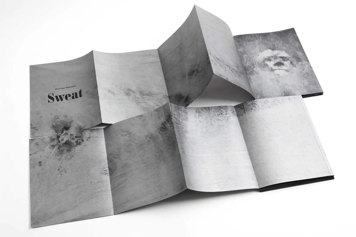 Accordion-fold art book laid open on a white surface, grayscale textures; left page features the word Sweat.