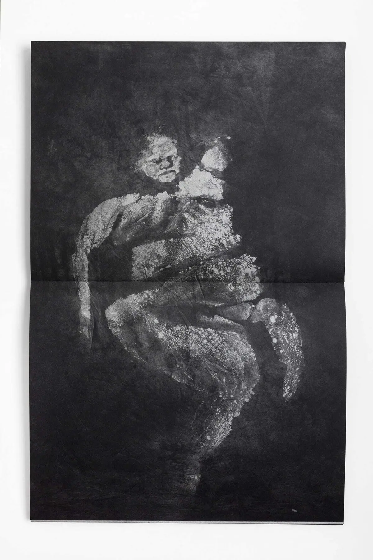Grayscale, grainy print of two people embracing against a dark backdrop.