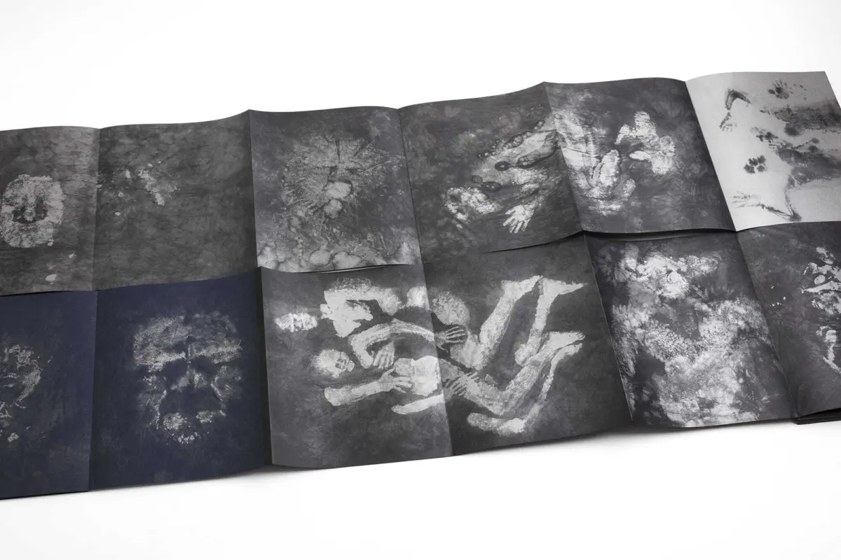 Accordion-folded grayscale prints on dark panels showing pale skeletal humans in intertwined, dynamic poses on a white surface.