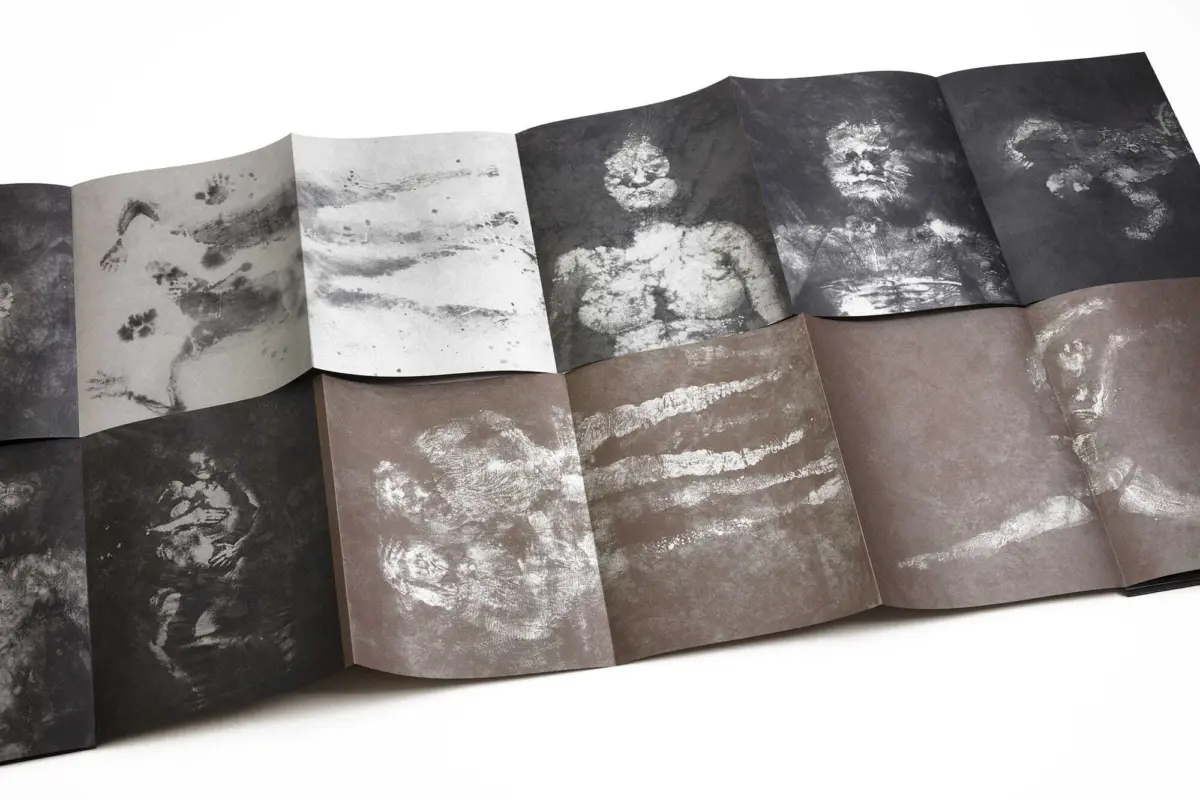 Accordion-style booklet pages in grayscale featuring white handprints on dark paper.