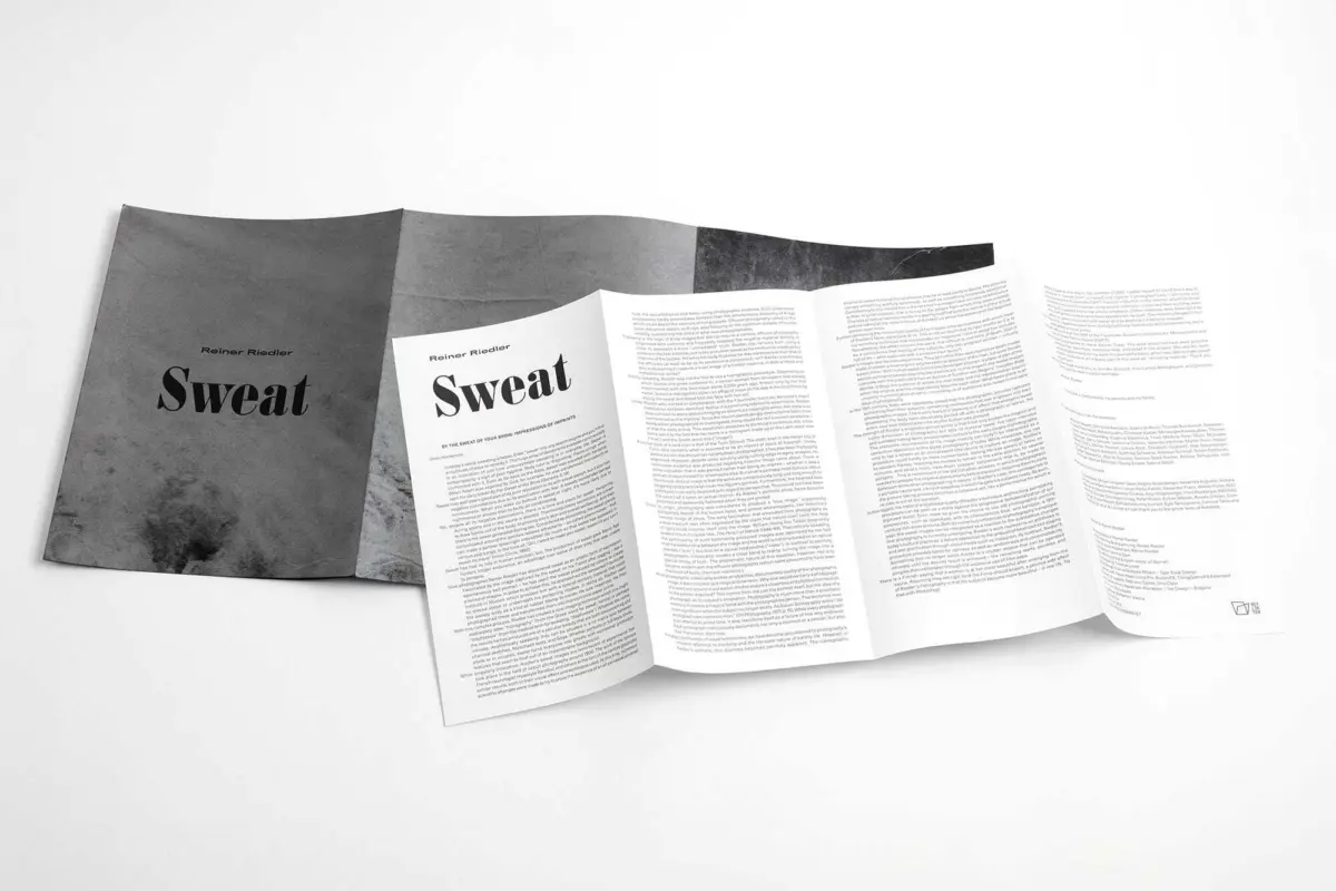 Dark-covered booklet titled Sweat, fanned open into white pages on a white surface.