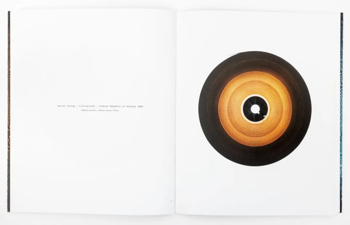 Open book spread; on the right page a large orange vinyl record with a black center hole, left page mostly blank with a small caption.