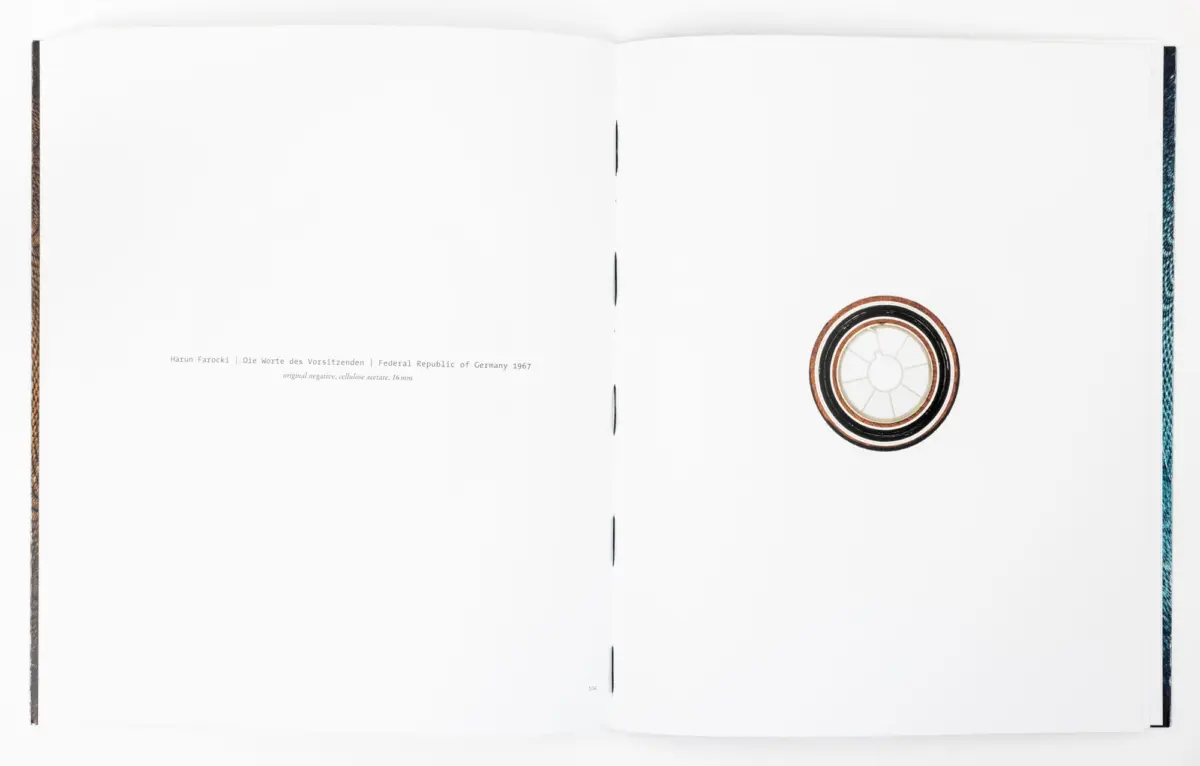 Open book with blank white pages; circular tape reel on the bottom-right of the right page.